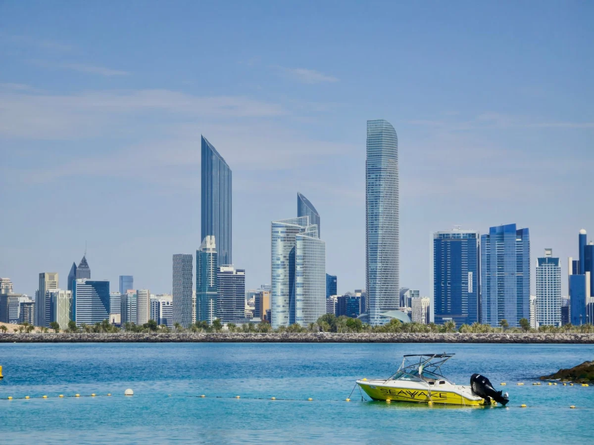 Vista vibrante dello skyline di Abu Dhabi con un motoscafo giallo sull'acqua calma e blu sotto un cielo limpido.
