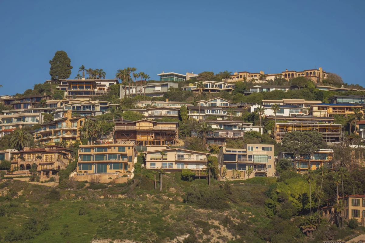 Scenic view of modern hillside homes with lush greenery and blue sky backdrop.