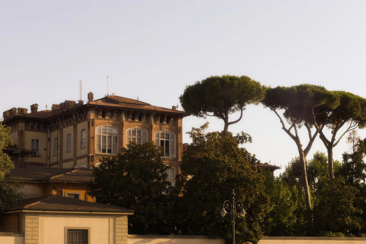 A charming historical villa in Pisa, Italy, framed by distinctive umbrella pine trees.