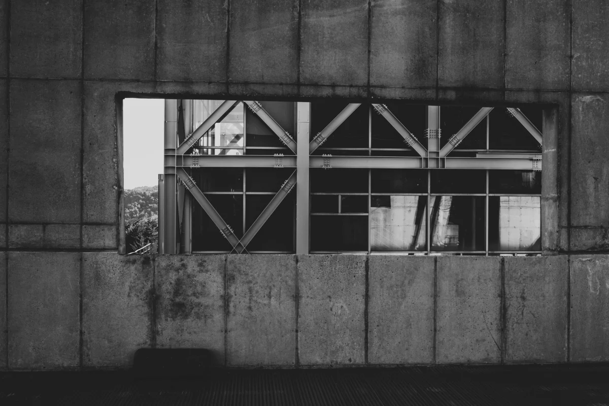 Foto in bianco e nero di travi strutturali moderne visibili attraverso un muro di cemento.