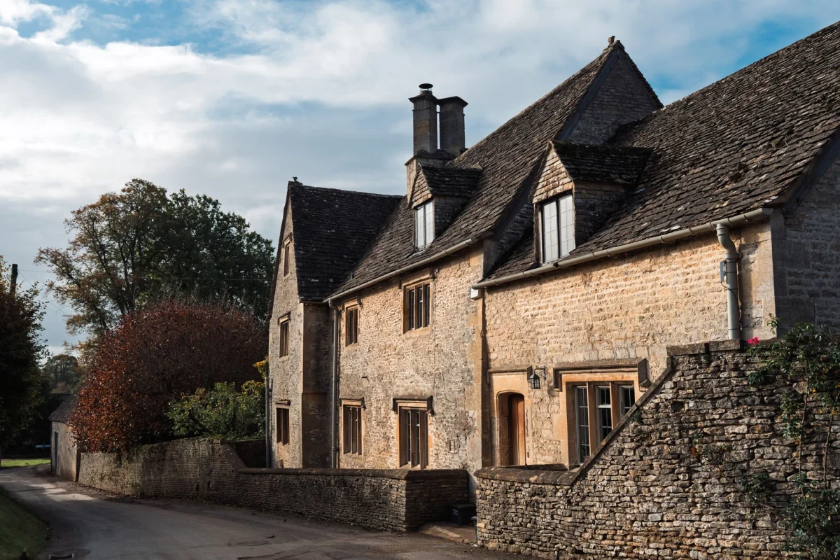 Picturesque Cotswold stone house with autumn trees, classic English countryside architecture.
