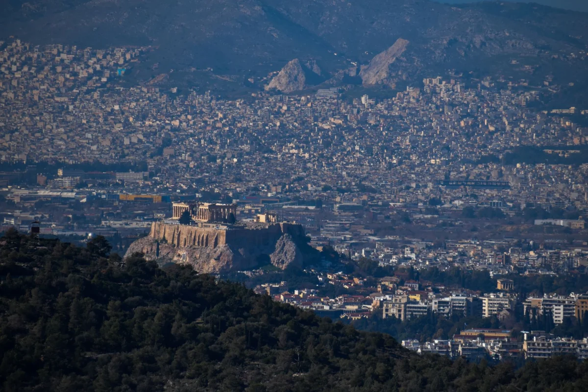 Stunning aerial shot of Athens cityscape with the Acropolis prominently visible, surrounded by urban sprawl and mountains.