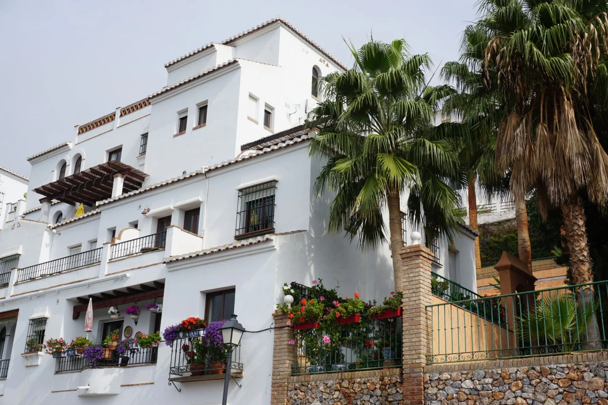 Elegant white villa surrounded by palm trees and vibrant flowers, showcasing Spanish architecture.